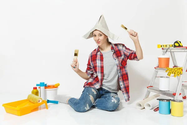 Mujer divertida en sombrero de periódico sentado en el suelo con cepillo, instrumentos para la renovación habitación del apartamento aislado sobre fondo blanco. Fondos de pantalla, accesorios para pegar, herramientas de pintura. Reparación concepto hogar . — Foto de Stock