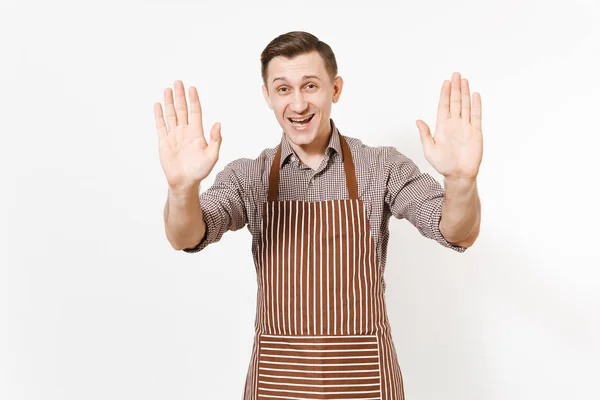 Joven hombre sonriente chef o camarero en delantal marrón rayado, camisa que muestra las palmas de las manos a la cámara aislada sobre fondo blanco. Hombre ama de llaves o empleada doméstica. Trabajadora doméstica con espacio de copia para publicidad . —  Fotos de Stock