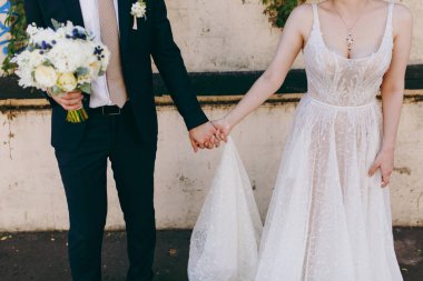 Güzel düğün kutlama. Buket ile takım elbiseli genç damat ve yaka çiçeği ve zarif dantel elbise eski arka plan üzerinde elele düzgün gelin duvar. Düğün giyim, Aksesuar