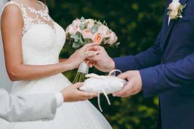 Güzel düğün kutlama. Damat bir yaka çiçeği ile mavi elbiseli yüzük onun gelin peçe ve peonies bir buket ile bir zarif dantel elbisesi koyar ve yeşil Bahçe, yeşil yaprakları