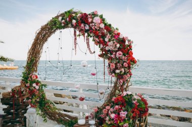 Güzel dekorasyon düğün töreni pembe, Bordo ve beyaz tonlarda ahşap iskele üzerinde. Yuvarlak kemerli ince dallarının çiçek kompozisyonlar gül ve peonies yanındaki mavi deniz ile dekore edilmiş