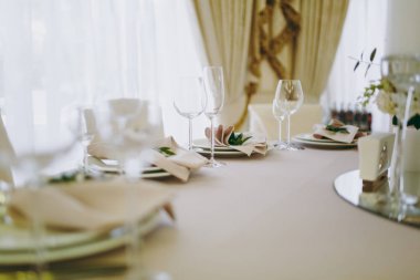 Güzel dekorasyon düğün Ziyafet içinde bir restoran pastel renklerde. Tablo hizmet bej masa örtüsü, tabaklar, gözlük, çatal bıçak takımı, peçete dekorasyon ile yeşil bir dal ile
