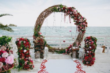 Güzel dekorasyon düğün töreni pembe, Bordo ve beyaz tonlarda ahşap iskele üzerinde. Yuvarlak kemerli ince dallarının çiçek kompozisyonlar gül ve peonies yanındaki mavi deniz ile dekore edilmiş