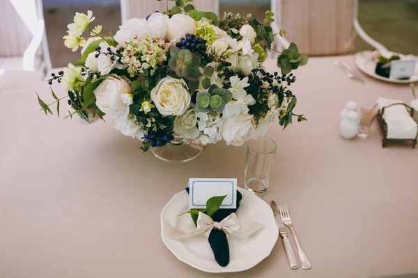 Mooie en verfijnde decoratie van de viering van de bruiloft in in het midden van een groene tuin. Banket geserveerd tafel met een beige tafelkleed, platen, servetten, kaarten en bloem composities — Stockfoto