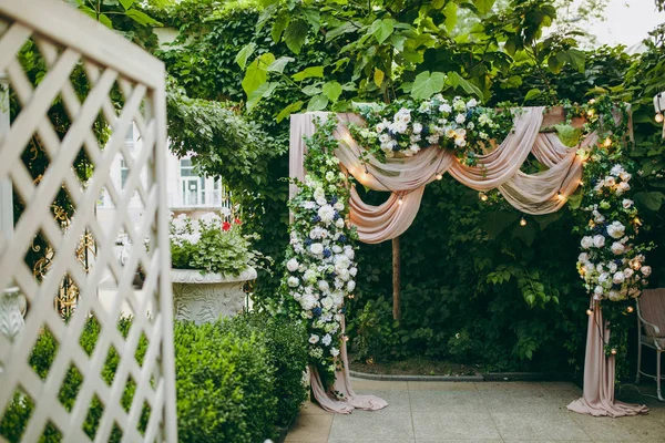 Schöne und exquisite Dekoration der Hochzeitsfeier inmitten eines grünen Gartens. hölzerner rechteckiger Rahmen mit rosa Tuch, vielen hellen Blumen und blauen Beeren dekoriert — Stockfoto