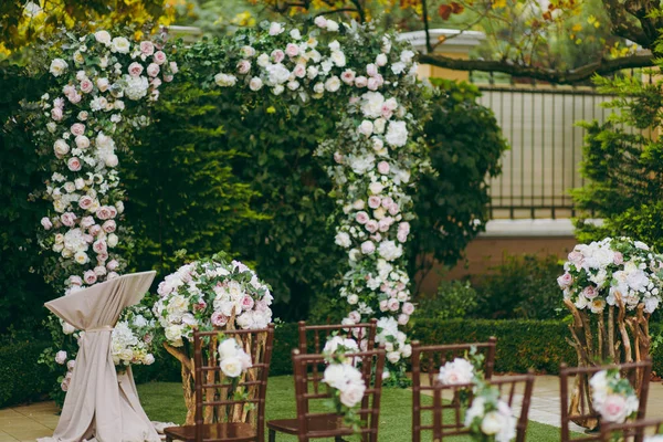Bela decoração de uma cerimônia de casamento em um jardim de outono verde. Cadeiras de madeira marrom para convidados de ambos os lados da passarela, o que leva a um arco festivo decorado com flores — Fotografia de Stock