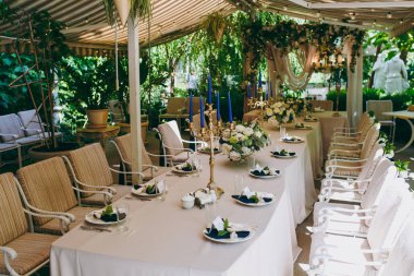 Güzel ve zarif dekorasyon düğün kutlama ortasında yeşil bir bahçe. Ziyafet masa örtü altında bej bir masa örtüsü, Kaplamalar ve şamdanlar mavi mum ile servis