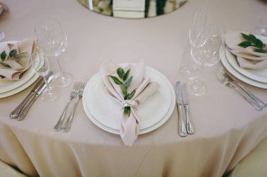 Güzel dekorasyon düğün Ziyafet içinde bir restoran pastel renklerde. Tablo hizmet bej masa örtüsü, tabaklar, gözlük, çatal bıçak takımı, peçete dekorasyon ile yeşil bir dal ile