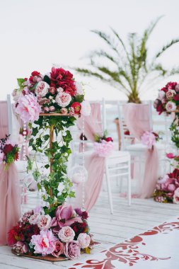 Güzel dekorasyon düğün töreni pembe, Bordo ve beyaz tonlarda ahşap iskele üzerinde. Sandalye dekore edilmiş ince bir bez, boncuk ve gül ve peonies çiçek kompozisyonlar