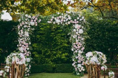 Güzel dekorasyon düğün töreni yeşil bir sonbahar Bahçe. Dikdörtgen kemer, narin pembe ve krem peonies ve dalları üzerinde çiçek kompozisyonlar yanında yeşil yaprakları ile süslenmiş