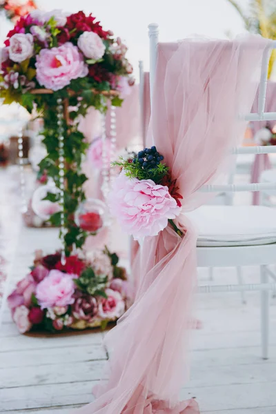 Beautiful decoration of the wedding ceremony in pink, burgundy and white tones on wooden pier. Chairs decorated with a thin cloth, beads and floral compositions of roses and peonies — Stock Photo, Image