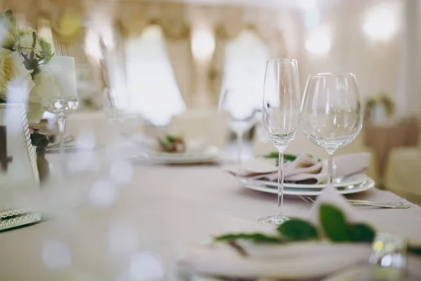 Красивое оформление свадебного банкета в ресторане в пастельных тонах. сервировка стола бежевой скатертью, тарелками, стаканами, столовыми приборами, украшением салфеток зеленой веточкой — стоковое фото