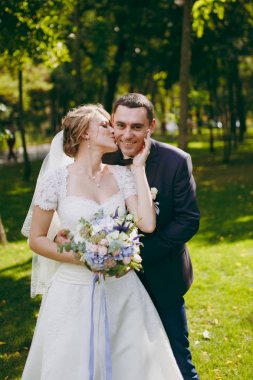 Güzel düğün photosession. Mavi resmi elbise ve elbise ve peçe kokulu güzel hairdress kucaklama güneşli büyük yeşil parkta bir yürüyüş ile onun zarif gelin yakışıklı damat