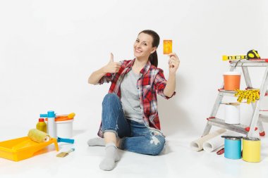 Beyaz arka plan üzerinde izole yenileme daire için aygıtlar ile katta oturan para ile kredi kartı tutan sevimli kadın. Boyama araçları yapıştırma için aksesuarları duvar kağıdı. Onarım ev concept.