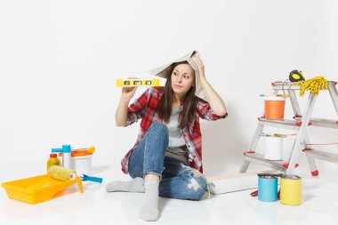 Oturan kat kabarcık ruh düzeyi ile beyaz arka plan üzerinde izole yenileme daire için aygıtlar üzerinde gazete şapkalı kadın. , Duvar kağıdı yapıştırma aksesuarları, boyama araçlarını. Onarım ev concept.