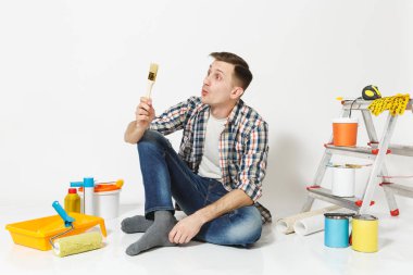 Eğlenceli kat boya fırçası ile yenileme daire oda için aygıtlar üzerinde oturan adam beyaz arka plan üzerinde izole mutlu gülümseyerek. , Duvar kağıdı yapıştırma aksesuarları, boyama araçlarını. Onarım ev concept.
