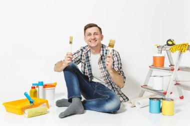 Eğlenceli kat boya fırçası ile yenileme daire oda için aygıtlar üzerinde oturan adam beyaz arka plan üzerinde izole mutlu gülümseyerek. , Duvar kağıdı yapıştırma aksesuarları, boyama araçlarını. Onarım ev concept.