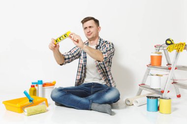 Kabarcık ruh düzeyi, beyaz arka plan üzerinde izole yenileme daire için aygıtlar bina ile katta oturan memnun şüpheci adam. Fer'î, alet yapıştırma duvar kağıdı. Onarım ev concept