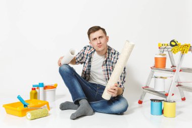 Rulo duvar kağıdı, beyaz arka plan üzerinde izole yenileme daire oda için aygıtlar ile katta oturan karışık rahatsız yorgun adam. Aksesuarlar, boyama araçlarını yapıştırma. Onarım ev concept.