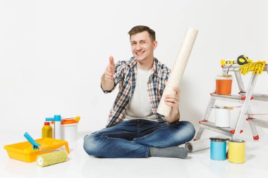 Tebrik için uzanmış el ile katta oturan genç adam. Beyaz arka plan üzerinde izole yenileme daire için aygıtlar. , Duvar kağıdı yapıştırma aksesuarları, boyama araçlarını. Onarım ev concept.