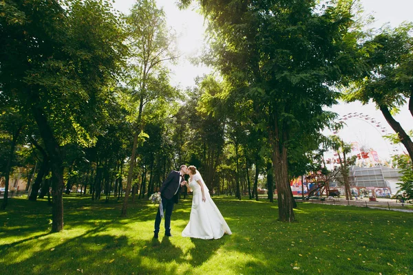 美丽的婚礼 photosession。英俊的新郎在蓝色正式西装与花束和他优雅的新娘在白色礼服和面纱与美丽的 hairdress 在一个晴朗的日子在大绿色公园散步 — 图库照片