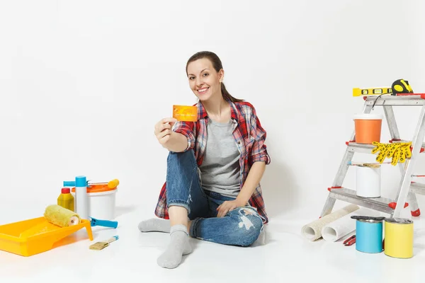 Nette Frau mit Kreditkarte und Geld auf dem Boden sitzend mit Instrumenten für die Renovierung Wohnung isoliert auf weißem Hintergrund. Tapeten-Zubehör zum Kleben von Malwerkzeugen. Heimkonzept reparieren. — Stockfoto