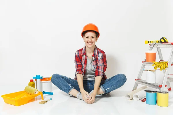 Woman in orange protective helmet sitting on floor with instruments for renovation apartment room isolated on white background. Wallpaper, accessories for gluing, painting tools. Repair home concept.