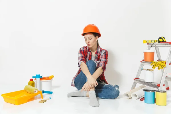 Συλλογισμένος γυναίκα στο πορτοκαλί προστατευτικό κράνος που κάθεται στο πάτωμα με τα όργανα για διαμέρισμα ανακαίνιση που απομονώνονται σε λευκό φόντο. Ταπετσαρία, αξεσουάρ για την κόλληση εργαλεία ζωγραφικής. Επισκευή concept home — Φωτογραφία Αρχείου