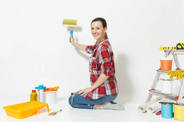 Pretty woman sitting on floor with paint roller, instruments for renovation apartment room isolated on white background. Wallpaper, accessories for gluing, painting wall tools. Repair home concept.