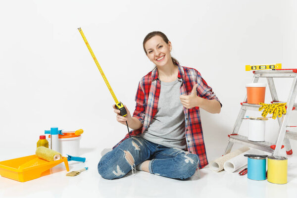 Woman in casual clothes sitting on floor with measure tape, instruments for renovation apartment isolated on white background. Wallpaper, accessories for gluing, painting tools. Repair home concept.