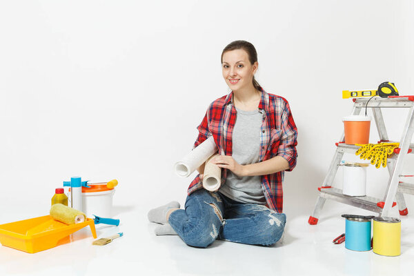 Woman in casual clothes sitting on floor with wallpaper rolls, instruments for renovation apartment isolated on white background. Accessories for gluing painting tools. Repair home concept. Copy space