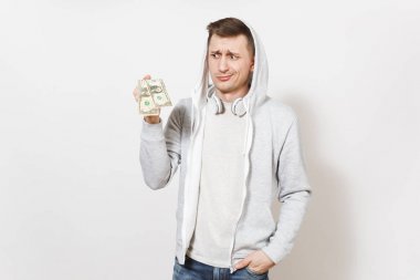 Genç yakışıklı erkek öğrenci tişört, kot ve kulaklık ile hood ile hafif kazak iki dolarlarına tutar ve perplexedly izole üzerinde beyaz arka plan görünüyor. Duygular kavramı