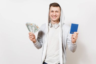 Mutlu adam t-shirt, kukuleta ile hafif sweatshirt içinde gülümseyen yakışıklı genç kulaklık uluslararası pasaport, dolar, demet izole beyaz arka plan üzerinde nakit para tutar. Seyahat, turizm kavramı