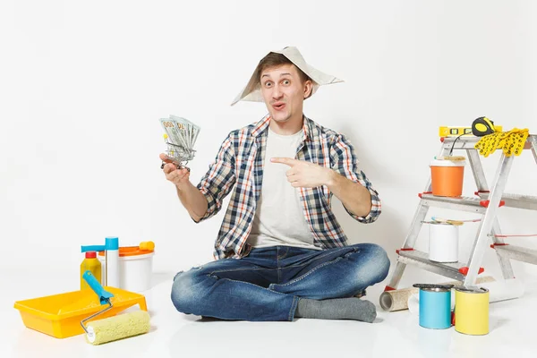 Ευτυχισμένος άνθρωπος στην εφημερίδα καπέλο κρατά δέσμη δολάρια, μετρητά χρήματα. Όργανα για διαμέρισμα ανακαίνιση που απομονώνονται σε λευκό φόντο. Ταπετσαρία, κόλλημα αξεσουάρ, εργαλεία βαφής. Επισκευή concept home. — Φωτογραφία Αρχείου