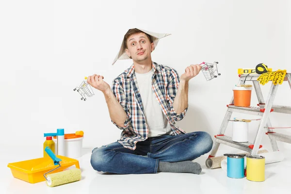 Homem feliz em chapéu de jornal detém supermercado carrinhos de supermercado empurrar para fazer compras. Instrumentos para renovação apartamento isolado em fundo branco. Papel de parede, acessórios para colar. Reparação home concept . — Fotografia de Stock