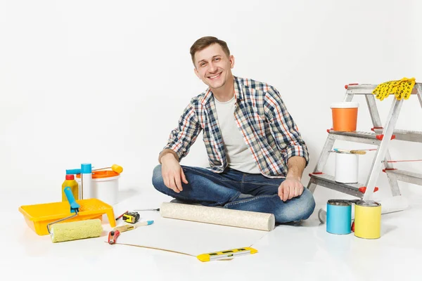 Duvar kağıdı rulo, kalem, beyaz arka plan üzerinde izole yenileme daire oda için aygıtlar ile katta oturan genç adam. , Duvar kağıdı yapıştırma aksesuarları, boyama araçlarını. Onarım ev concept.