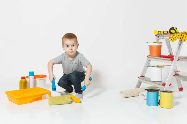 Маленький милый мальчик стоит с инструментами для ремонта квартиры комнату изолированы на белом фоне. Обои, клеящие аксессуары, инструменты для покраски. Сын чинит дом. Родительство, концепция детства . — стоковое фото