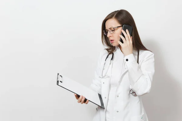 Mujer doctora seria con estetoscopio, gafas aisladas sobre fondo blanco. Doctora en bata médica hablar en el teléfono móvil, mantenga la tarjeta de salud en la carpeta del bloc de notas. Concepto de personal sanitario . — Foto de Stock