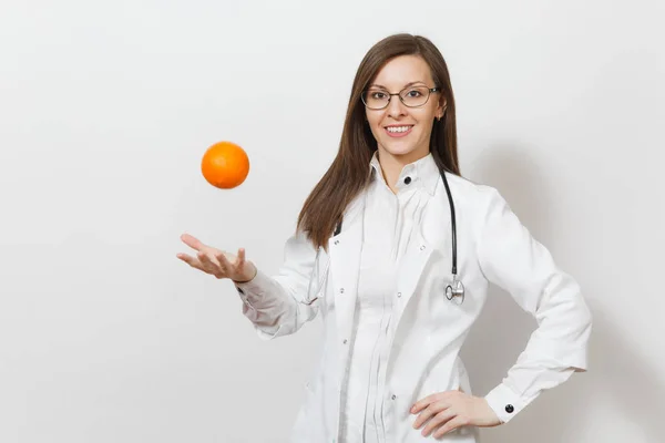 Sonriente mujer doctora joven y segura de sí misma con estetoscopio, gafas aisladas sobre fondo blanco. Doctora en bata médica vomitando naranja. Personal sanitario, salud, concepto de medicina . — Foto de Stock