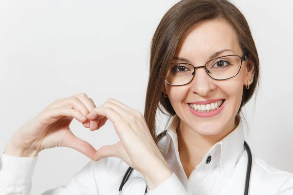 Close up sorridente donna medico attraente con stetoscopio, occhiali isolati su sfondo bianco. Medico donna in uniforme medica che mostra la forma del cuore con le mani. Personale sanitario, concetto di medicina — Foto Stock