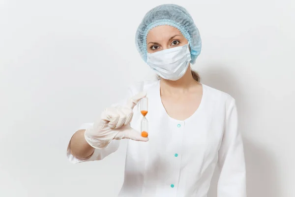 Unga läkare kvinna med ansiktsmask, sterila hatt, handskar isolerad på vit bakgrund. Kvinnliga kirurgen läkare i medicinsk klänning innehar timglas. Vårdpersonal, medicin koncept. Tiden rinner ut. — Stockfoto