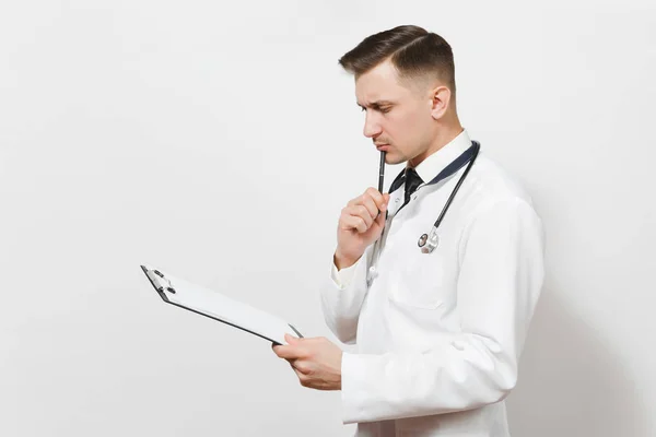 Серьезный задумчивый привлекательный молодой доктор, изолированный на белом фоне. Мужчина-врач в медицинской форме, медицинская карта стетоскопа на папке блокнота. Медицинская концепция медицинского персонала . — стоковое фото