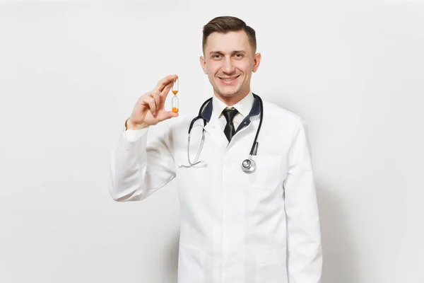 Χαμογελαστός άνθρωπος όμορφος νεαρός γιατρός που απομονώνονται σε λευκό φόντο. Αρσενικό ιατρός στην ιατρική στολή, στηθοσκόπιο κρατώντας κλεψύδρα. Νοσηλευτικού προσωπικού, την υγεία, την ιατρική έννοια. Ο χρόνος εξαντλείται. — Φωτογραφία Αρχείου