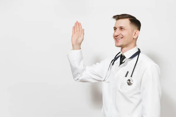 Sorridente felice bel giovane medico isolato su sfondo bianco. Medico maschio in uniforme medica, stetoscopio guardando da parte, agitando la mano per il saluto. Concetto di medicina sanitaria del personale sanitario . — Foto Stock