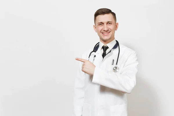 Sorridente bel giovane medico isolato su sfondo bianco. Medico maschio in abito medico, stetoscopio indicando dito indice da parte su spazio copia. Personale sanitario, salute, concetto di medicina . — Foto Stock
