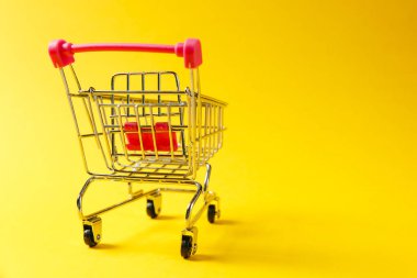 Süpermarket bakkal itme sepetinin siyah jantlar ve tutamacı üzerinde sarı arka plan izole kırmızı plastik öğelerle birlikte alışveriş için kapatın. Alışveriş kavramı. Kopya alanı reklam için