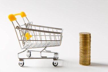 Süpermarket bakkal itme sepeti ile sarı plastik saplı sonraki beyaz arka plan üzerinde izole altın sikke yığını için alışveriş için kapatın. Alışveriş, para kavramı. Kopya alanı reklam için