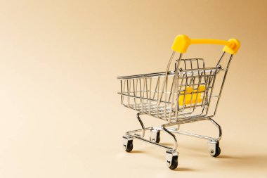 Süpermarket bakkal itme sepetinin siyah jantlar ve tutamacı üzerinde bej arka plan izole sarı plastik öğelerle birlikte alışveriş için kapatın. Alışveriş kavramı. Kopya alanı reklam için