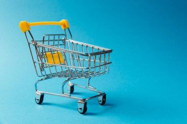 Süpermarket bakkal itme sepetinin siyah jantlar ve tutamacı üzerinde mavi arka plan izole sarı plastik öğelerle birlikte alışveriş için kapatın. Alışveriş kavramı. Kopya alanı reklam için
