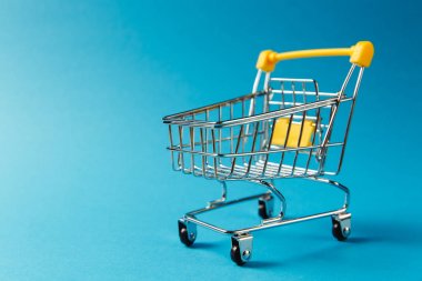 Süpermarket bakkal itme sepetinin siyah jantlar ve tutamacı üzerinde mavi arka plan izole sarı plastik öğelerle birlikte alışveriş için kapatın. Alışveriş kavramı. Kopya alanı reklam için